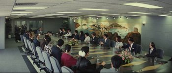 Movie still from “Police Story 2” (1988), directed by Jackie Chan – A group of people sitting around a table in a room; Wide shot, High angle