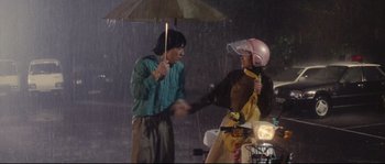 Movie still from “Police Story 2” (1988), directed by Jackie Chan – A man holding an umbrella and a woman holding an umbrella in the rain; Medium shot, Low angle