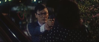 Movie still from “Police Story 2” (1988), directed by Jackie Chan – A man holding a gun pointed at a woman; Close Up shot, Over the shoulder angle