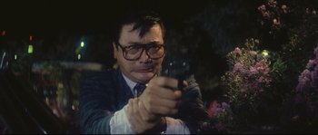 Movie still from “Police Story 2” (1988), directed by Jackie Chan – A man holding a gun while wearing glasses; Close Up shot, Low angle