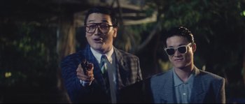 Movie still from “Police Story 2” (1988), directed by Jackie Chan – A man in a suit and tie holding a gun; Medium shot, Low angle