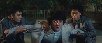 Movie still from “Police Story 2” (1988), directed by Jackie Chan – A man in a white shirt and blue shirt is holding another man in a white shirt; Medium shot, Low angle