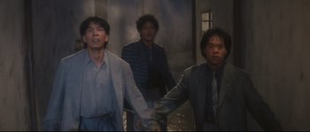 Movie still from “Police Story 2” (1988), directed by Jackie Chan – A group of people holding hands in a room; Medium shot, Low angle