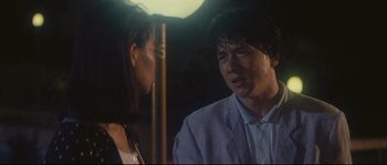 Movie still from “Police Story 2” (1988), directed by Jackie Chan – A man and a woman standing next to each other in front of an umbrella; Close Up shot, Over the shoulder angle
