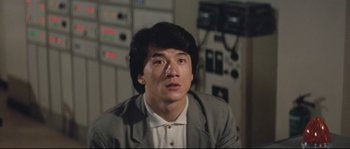 Movie still from “Police Story 2” (1988), directed by Jackie Chan – A man in a suit and tie in front of a wall; Close Up shot, Low angle