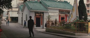 Movie still from “Police Story 2” (1988), directed by Jackie Chan – A man standing in front of a building with green roof; Extreme Wide shot, High angle
