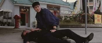 Movie still from “Police Story 2” (1988), directed by Jackie Chan – A man kneeling down next to another man on the ground; Medium shot, High angle