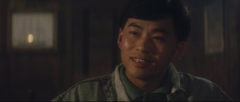 Movie still from “Police Story 2” (1988), directed by Jackie Chan – A person smiling for the camera; Close Up shot, Over the shoulder angle