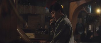 Movie still from “Police Story 2” (1988), directed by Jackie Chan – A man sitting at a table talking on a phone; Medium shot, High angle