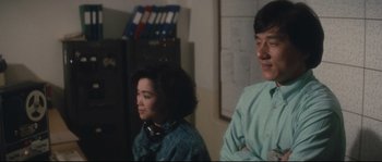 Movie still from “Police Story 2” (1988), directed by Jackie Chan – A man and a woman standing next to each other in a room; Medium shot, Over the shoulder angle