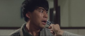 Movie still from “Police Story 2” (1988), directed by Jackie Chan – A man crying while holding a gun in his hand; Close Up shot, High angle
