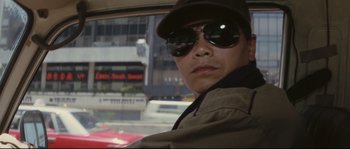 Movie still from “Police Story 2” (1988), directed by Jackie Chan – A man wearing a hat and sunglasses in a car; Close Up shot, Low angle