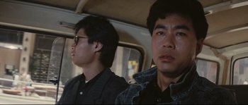 Movie still from “Police Story 2” (1988), directed by Jackie Chan – Two men sitting in the back seat of a car; Close Up shot, Low angle