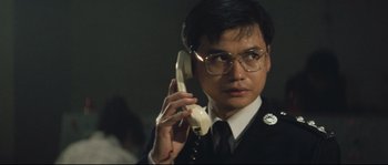 Movie still from “Police Story 2” (1988), directed by Jackie Chan – A man wearing a suit and glasses talking on a phone; Close Up shot, Low angle