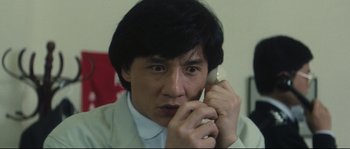 Movie still from “Police Story 2” (1988), directed by Jackie Chan – A man talking on a cell phone while wearing a suit; Close Up shot, Low angle