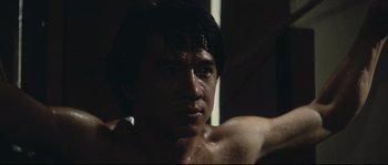 Movie still from “Police Story 2” (1988), directed by Jackie Chan – A shirtless man with wet hair in a dark room; Close Up shot, Low angle
