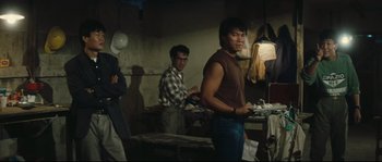 Movie still from “Police Story 2” (1988), directed by Jackie Chan – A group of people standing around in a room; Medium shot, Over the shoulder angle