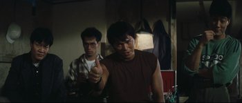 Movie still from “Police Story 2” (1988), directed by Jackie Chan – A man in a brown shirt is giving the middle finger; Medium shot, Low angle