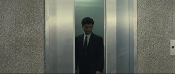 Movie still from “Police Story 2” (1988), directed by Jackie Chan – A man wearing a suit and tie standing in front of an elevator; Wide shot, Low angle