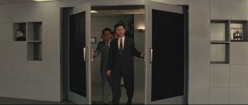 Movie still from “Police Story 2” (1988), directed by Jackie Chan – Two men in business suits are walking through a doorway; Medium shot, Low angle