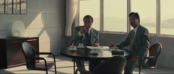 Movie still from “Police Story 2” (1988), directed by Jackie Chan – A man sitting at a table in front of two other men; Medium shot, Over the shoulder angle