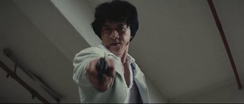 Movie still from “Police Story 2” (1988), directed by Jackie Chan – A man holding a gun pointed at the camera; Close Up shot, Low angle