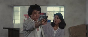 Movie still from “Police Story 2” (1988), directed by Jackie Chan – A man and a woman holding a gun in front of a window; Medium shot, High angle