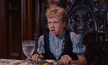 Movie still from “Pollyanna” (1960), directed by David Swift – A young girl sitting at a table with a plate in front of her mouth; Close Up shot, High angle
