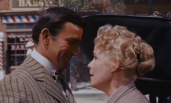 Movie still from “Pollyanna” (1960), directed by David Swift – A man and a woman standing next to each other in front of an umbrella; Close Up shot, Over the shoulder angle
