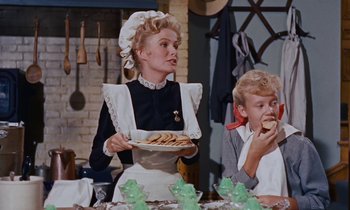 Movie still from “Pollyanna” (1960), directed by David Swift – A woman holding a plate of food while a boy eats a piece of bread; Medium shot, Over the shoulder angle