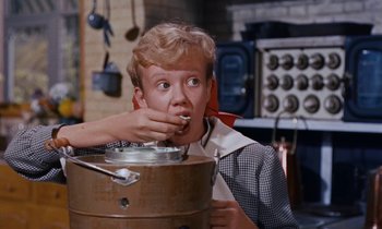 Movie still from “Pollyanna” (1960), directed by David Swift – A young man eating something while sitting on a barrel; Medium shot, Low angle