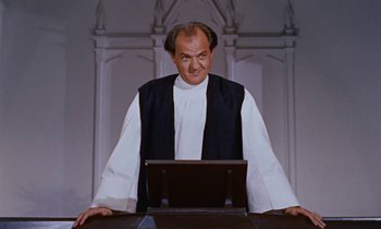 Movie still from “Pollyanna” (1960), directed by David Swift – A man wearing a black vest and a black vest standing in front of an open laptop computer; Medium shot, Low angle