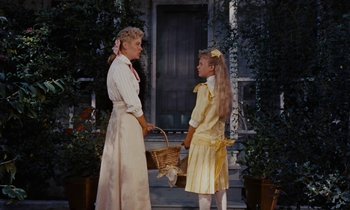 Movie still from “Pollyanna” (1960), directed by David Swift – Two girls in dresses stand on the porch of a house; Medium shot, Low angle