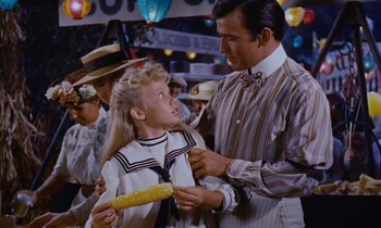 Movie still from “Pollyanna” (1960), directed by David Swift – A man and a little girl are standing in front of a crowd; Medium shot, Over the shoulder angle
