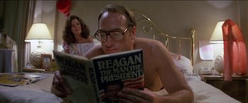 Movie still from “Poltergeist” (1982), directed by Tobe Hooper – A man reading a book in bed with a woman in the background; Medium shot, High angle