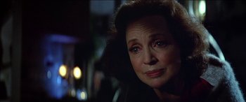 Movie still from “Poltergeist” (1982), directed by Tobe Hooper – An older woman looking at the camera in a dimly - lit room; Close Up shot, Over the shoulder angle