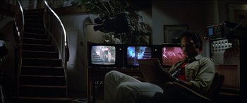 Movie still from “Poltergeist” (1982), directed by Tobe Hooper – A man sitting on a couch in front of three televisions; Wide shot, Over the shoulder angle