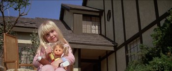 Movie still from “Poltergeist” (1982), directed by Tobe Hooper – A little girl holding a doll in front of a house; Close Up shot, Low angle