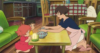 Movie still from “Ponyo” (2008), directed by Hayao Miyazaki – Two children and an adult sitting at a table in a kitchen; Wide shot, High angle