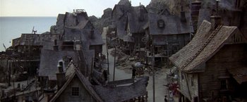 Movie still from “Popeye” (1980), directed by Robert Altman – An aerial view of a town with many buildings and stairs; Extreme Wide shot, High angle