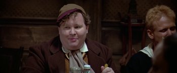 Movie still from “Popeye” (1980), directed by Robert Altman – A man in a brown jacket and a brown hat holding food; Close Up shot, Over the shoulder angle