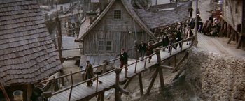 Movie still from “Popeye” (1980), directed by Robert Altman – A group of people walking down a wooden bridge; Extreme Wide shot, High angle