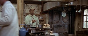 Movie still from “Popeye” (1980), directed by Robert Altman – A man standing in front of a table in a kitchen; Medium shot, Over the shoulder angle