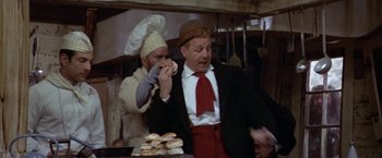Movie still from “Popeye” (1980), directed by Robert Altman – A man in a suit and a hat is eating a sandwich; Medium shot, Low angle