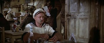Movie still from “Popeye” (1980), directed by Robert Altman – A man sitting at a table eating a sandwich; Close Up shot, Low angle