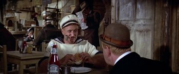 Movie still from “Popeye” (1980), directed by Robert Altman – Two men sitting at a table eating a sandwich; Close Up shot, Over the shoulder angle