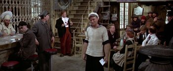 Movie still from “Popeye” (1980), directed by Robert Altman – A man in a sailor's outfit standing in front of other men; Wide shot, High angle