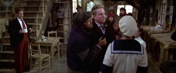Movie still from “Popeye” (1980), directed by Robert Altman – Two men are hugging each other in front of a group of people; Medium shot, Over the shoulder angle