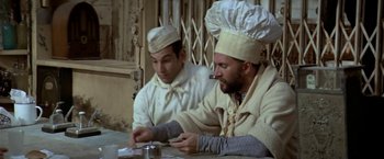 Movie still from “Popeye” (1980), directed by Robert Altman – Two men in chef's hats are sitting at a table; Medium shot, Low angle