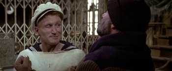 Movie still from “Popeye” (1980), directed by Robert Altman – A man in a sailor's uniform talking to another man; Close Up shot, Over the shoulder angle